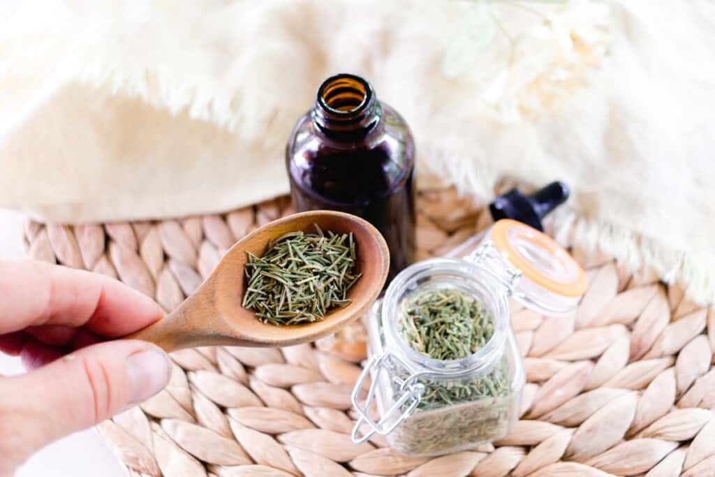 A spoonful of dried Rosemary with glass bottle nearby.