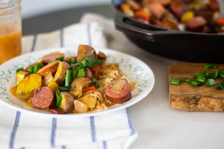 Delicious plate of sausage and potatoes over dirty rice with spicy gravy drizzled overtop.