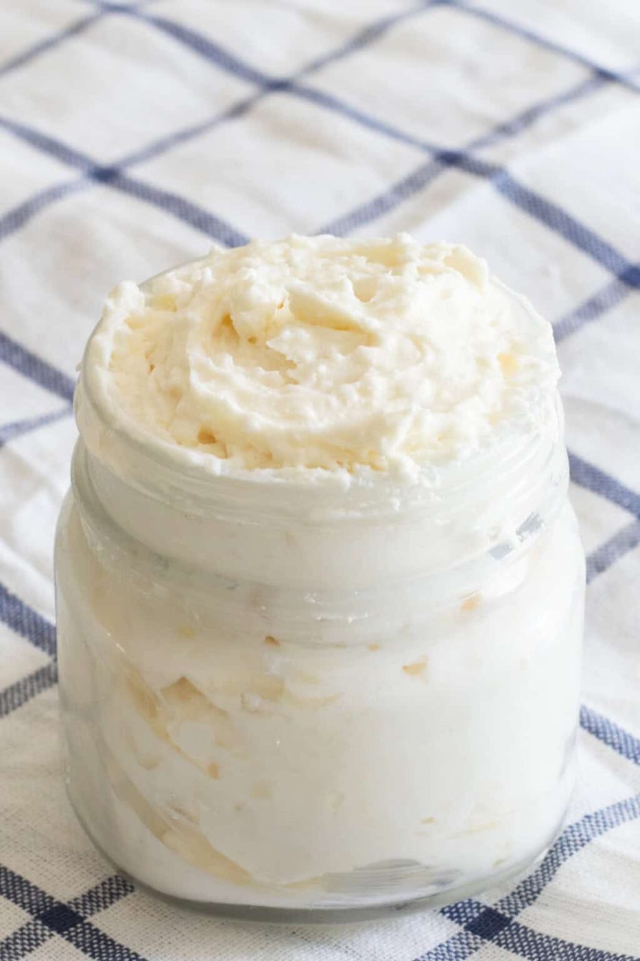 A jar of homemade shea butter lotion on a checkered blue tablecloth.