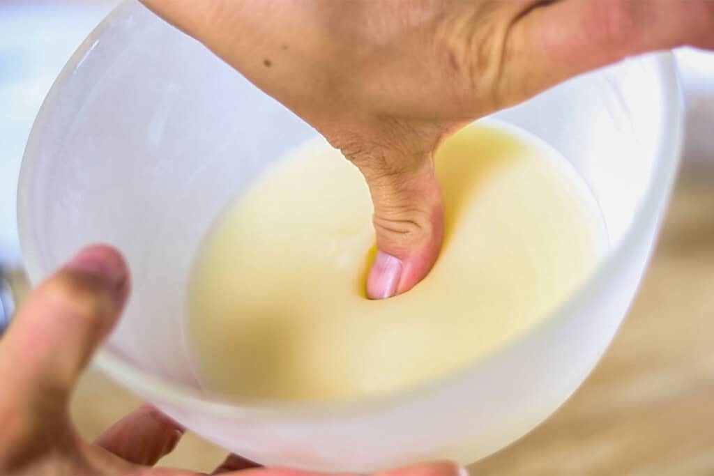 Pressing a fingertip into a bowl of hardened lotion mixture.