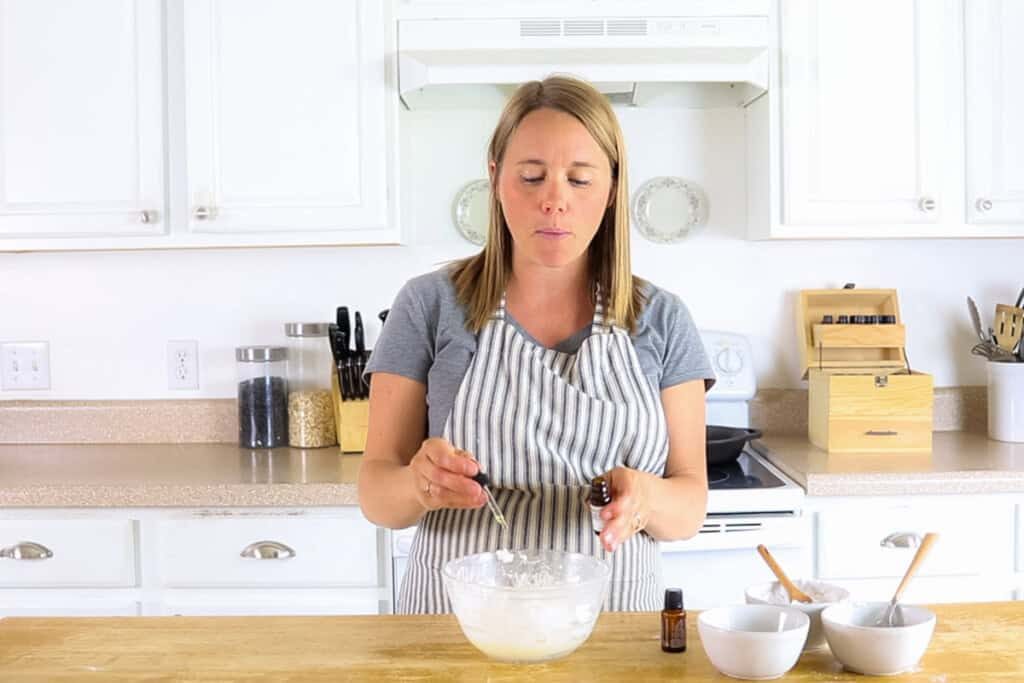 Adding essential oils into a glass bowl of lotion mixture with a dropper.