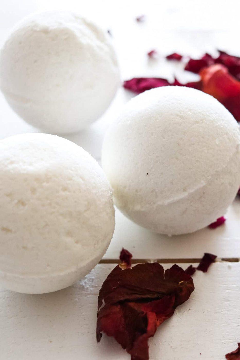 3 homemade bath bombs on a white table with rose petals surrounding it.