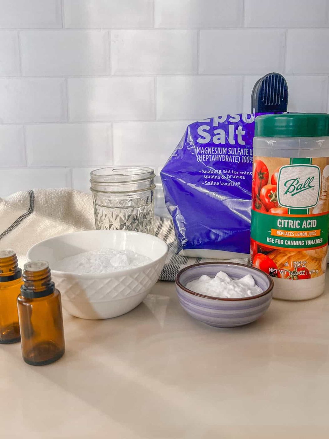 Ingredients for a bath bomb recipe measured out on a white marble vanity.