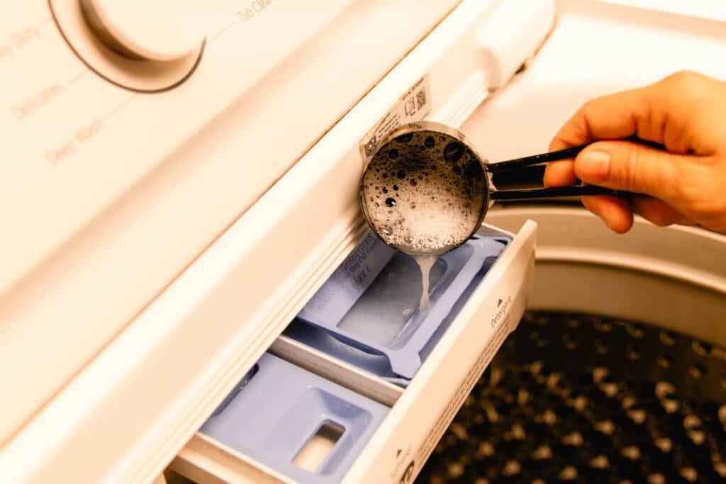 Pouring homemade laundry detergent into the soap tray of a washing machine.