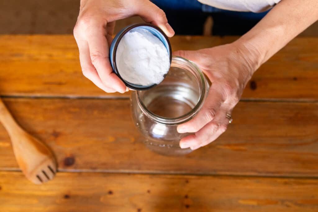 Pouring baking soda into the glass jar with water.
