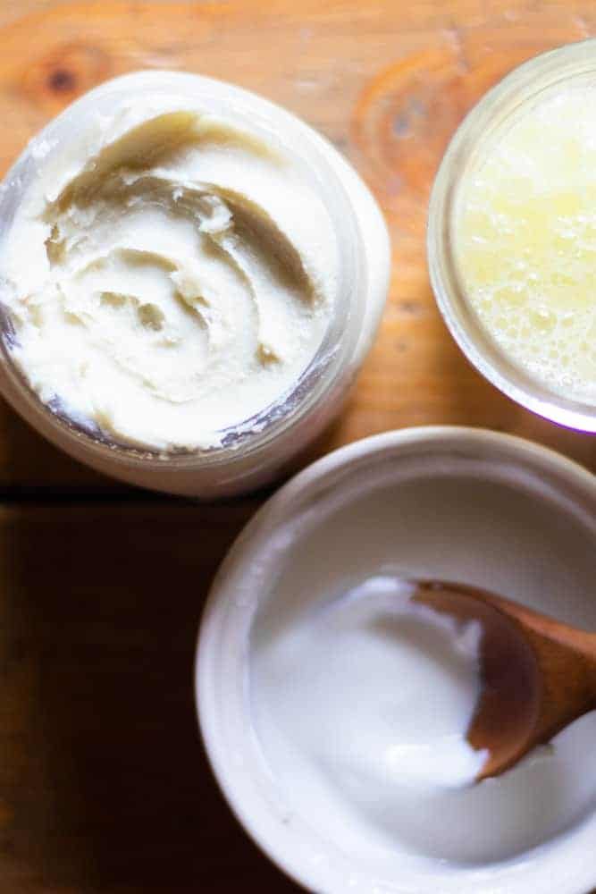 Three jars of homemade skincare products sitting on wooden board.