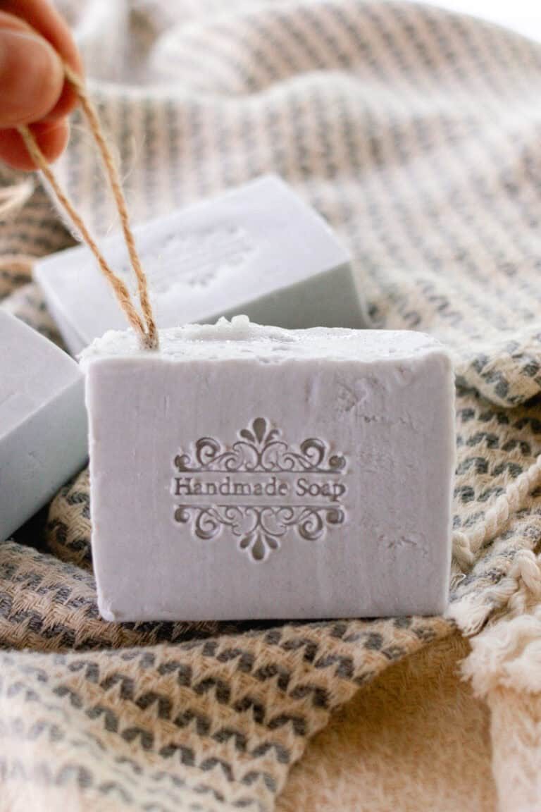 A handmade soap on a rope bar sitting on a towel. The bar is stamped with "handmade soap" on the front.