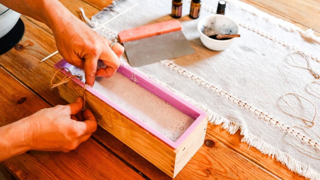 Adding the tied jute string loops into the soap while it is still melted in the soap mold.