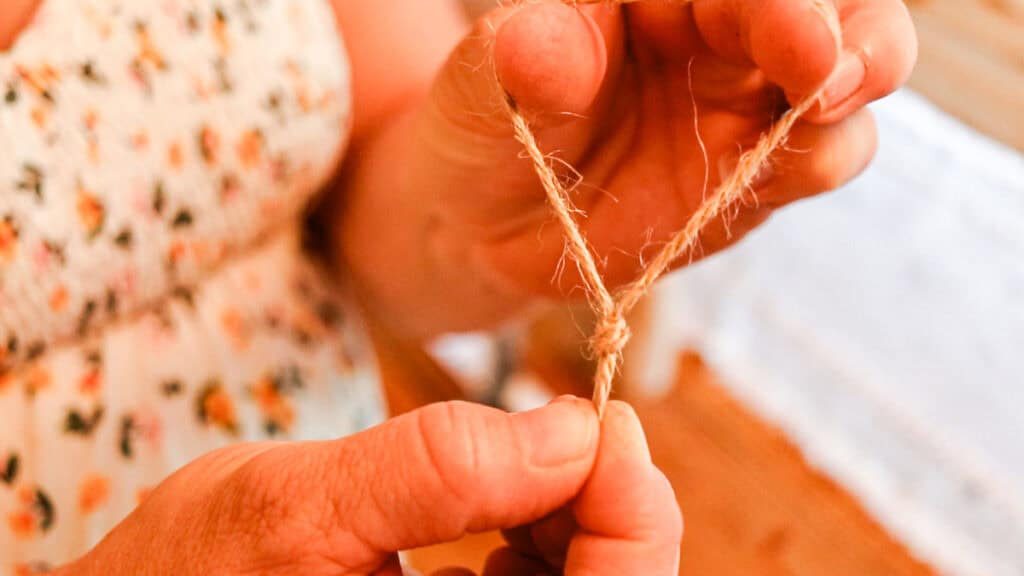 Hands tying a jute string into a loop with a knot at the end.