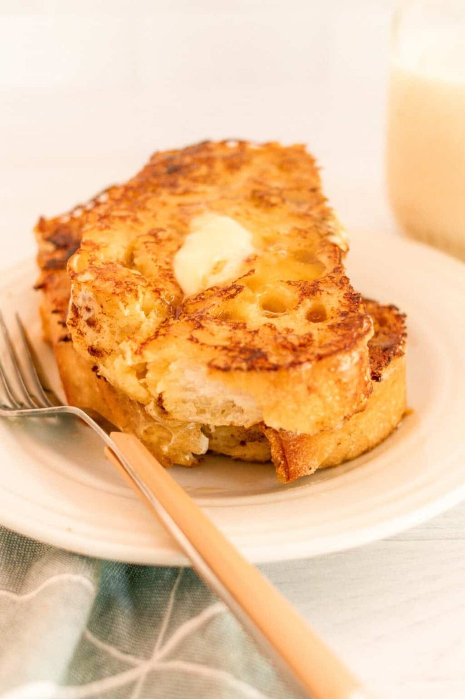 A white plate with a fork and sourdough french toast with butter.