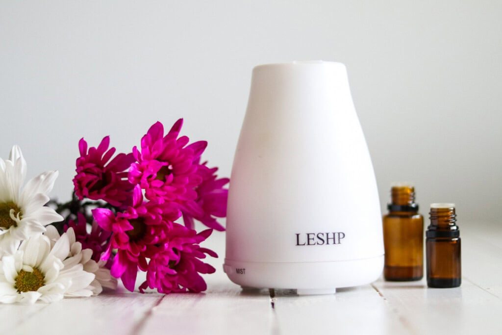 An essential oil diffuser with bottles of oil and pink flowers.