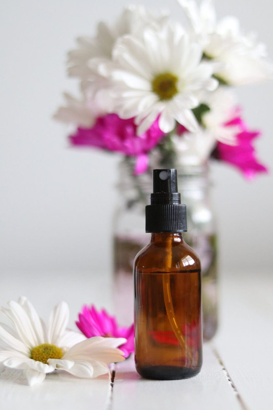 An amber glass bottle of spring room spray with white and pink flowers in the background.
