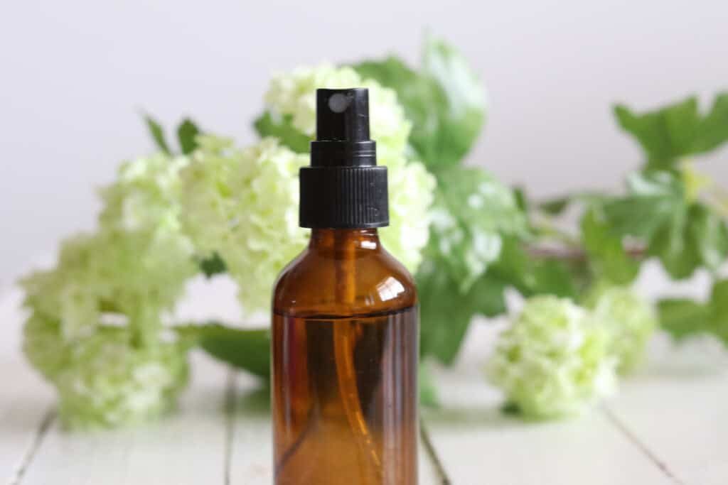 An amber spray bottle with fresh flowers around it.