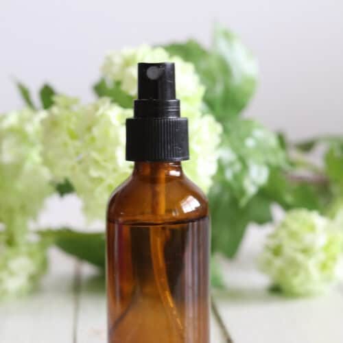 An amber spray bottle with fresh flowers around it.