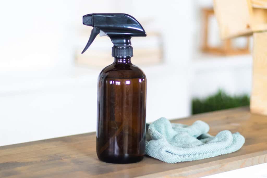 A spray bottle with a microfiber cloth on a wooden table.