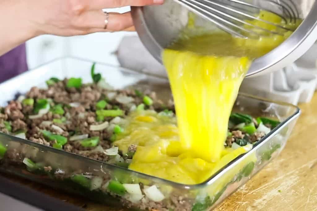 Pouring eggs into a sweet potato breakfast casserole.