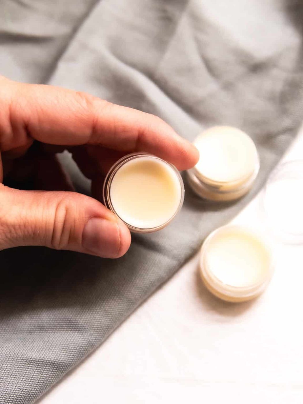 Holding a container of tallow lip balm with more containers in the background.