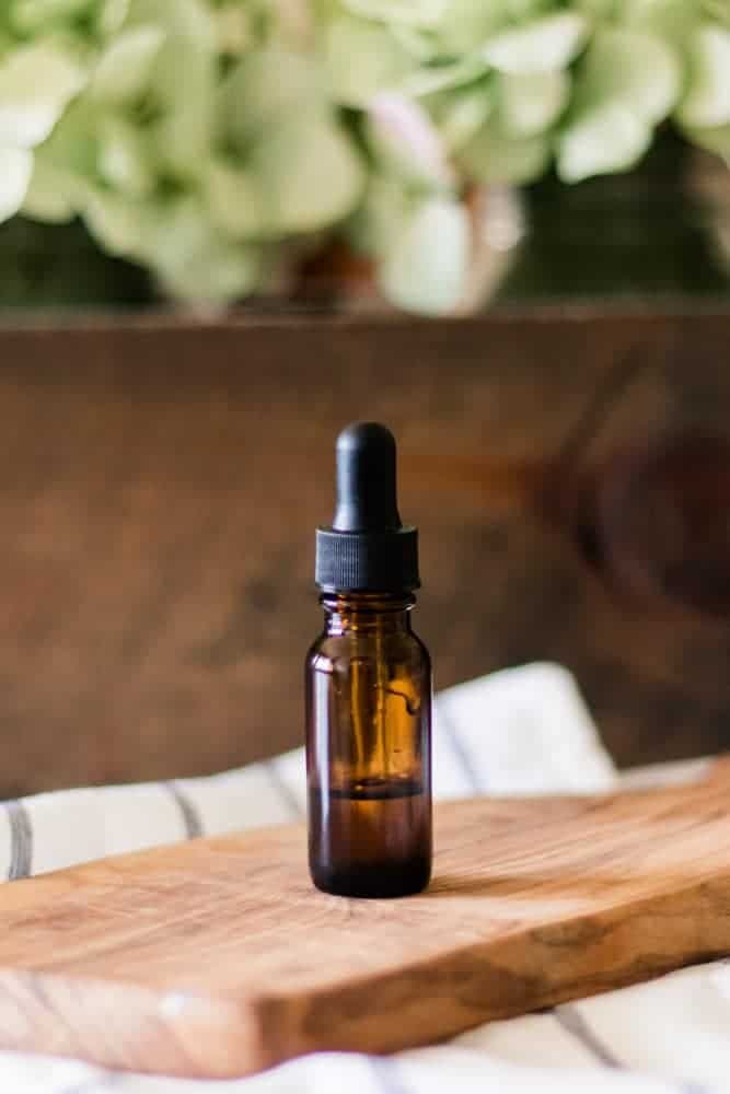 Vitamin E oil bottle standing on a wooden cutting board with green flowers behind it.