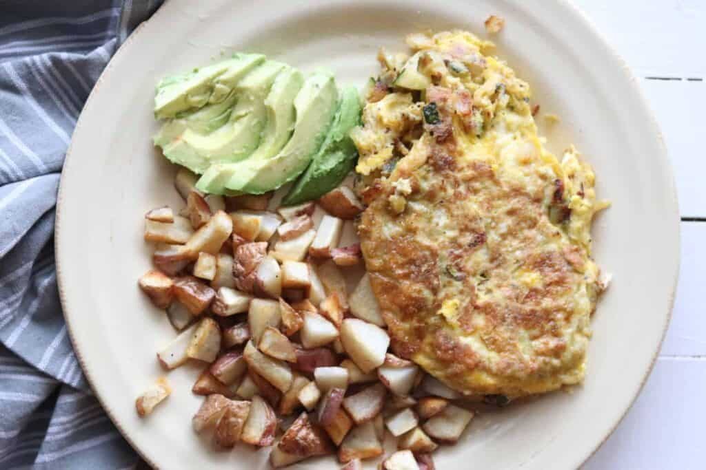 Vegetable omelet, hash browns and sliced avocado.
