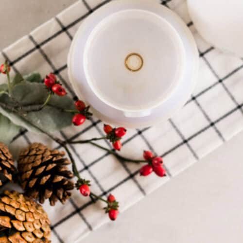 Looking down on a diffuser, red berries, and pinecones on a plaid towel.
