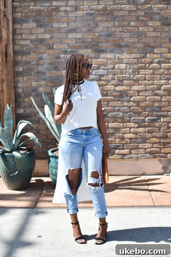 Woman in ripped jeans and high-low top, posing with a leather clutch and chunky velvet heels.