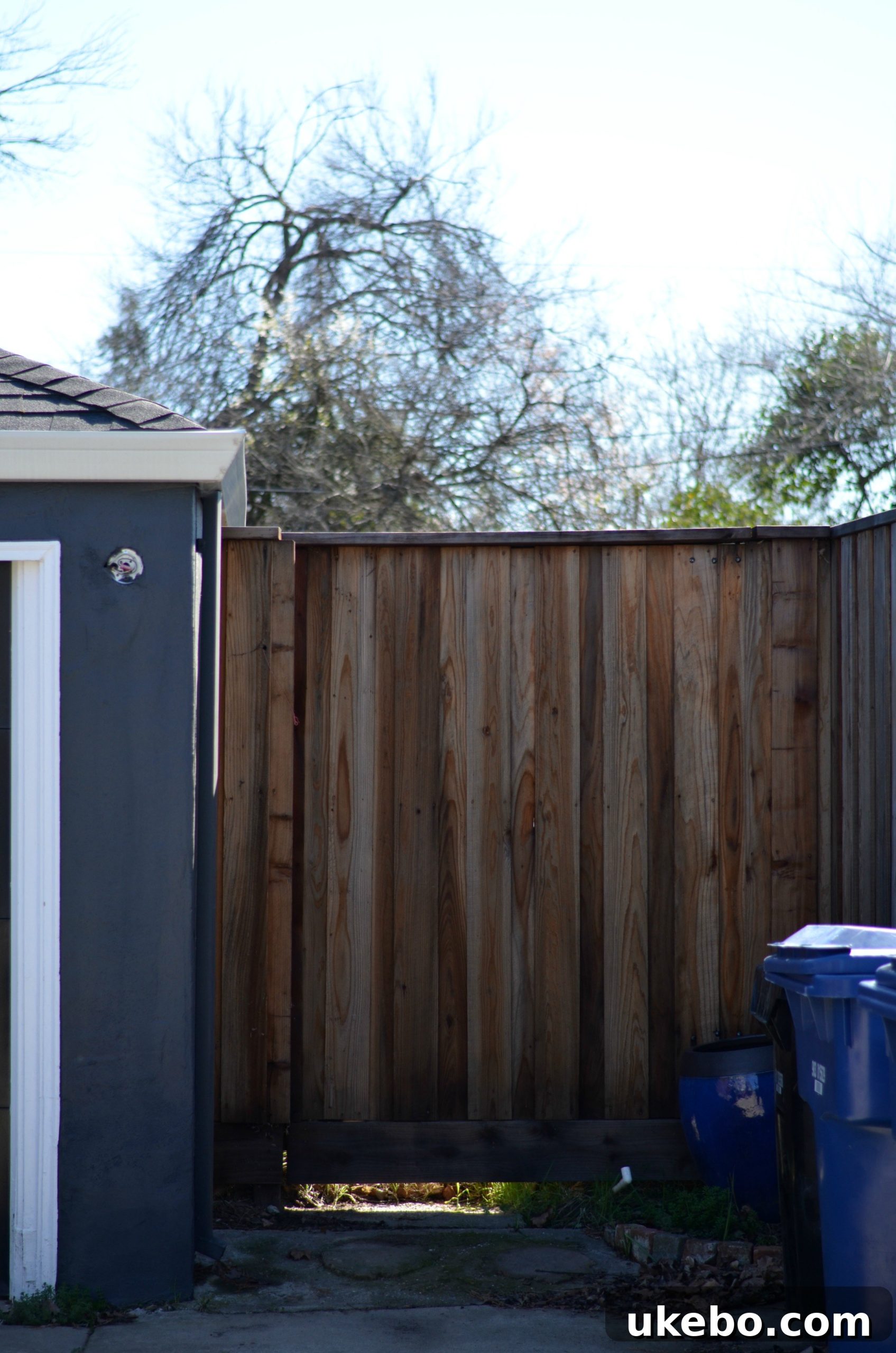 New wide redwood gate creating a dedicated storage area for waste bins beside the garage.