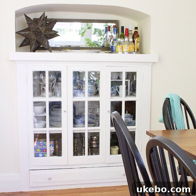 Cozy dining room featuring abundant natural light, a built-in china cabinet with glass doors, and a decorative Spanish-style niche, radiating warmth and charm.
