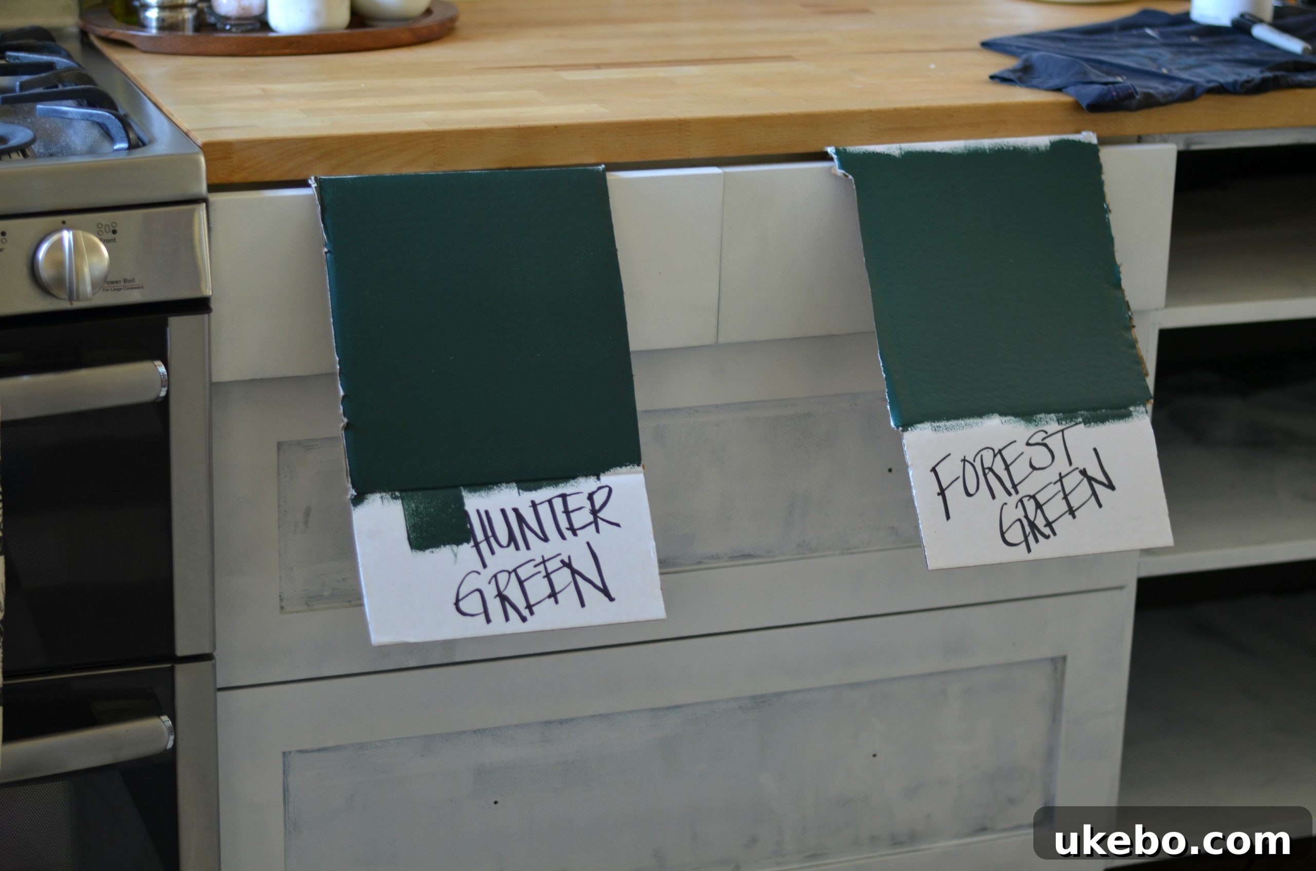 Paint swatches of Benjamin Moore Hunter Green and Forest Green on kitchen cabinets