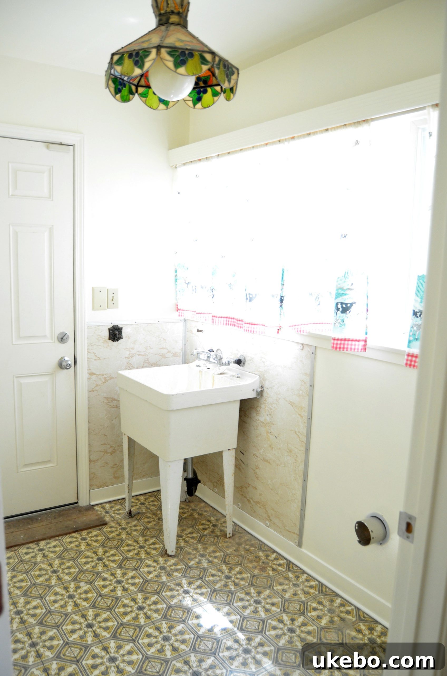 Before image of a cluttered and outdated laundry room with beige walls and old flooring.