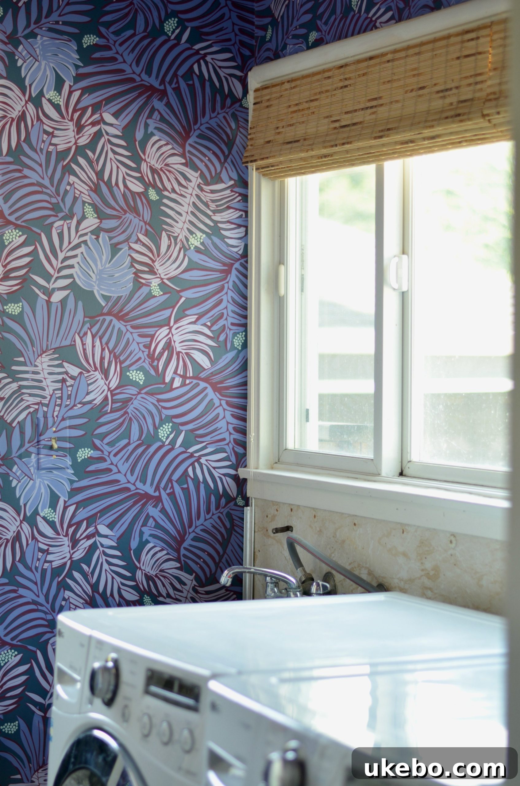 Laundry room interior showcasing the seamless application of wallpaper on both walls and ceiling, with bamboo shades on the window.