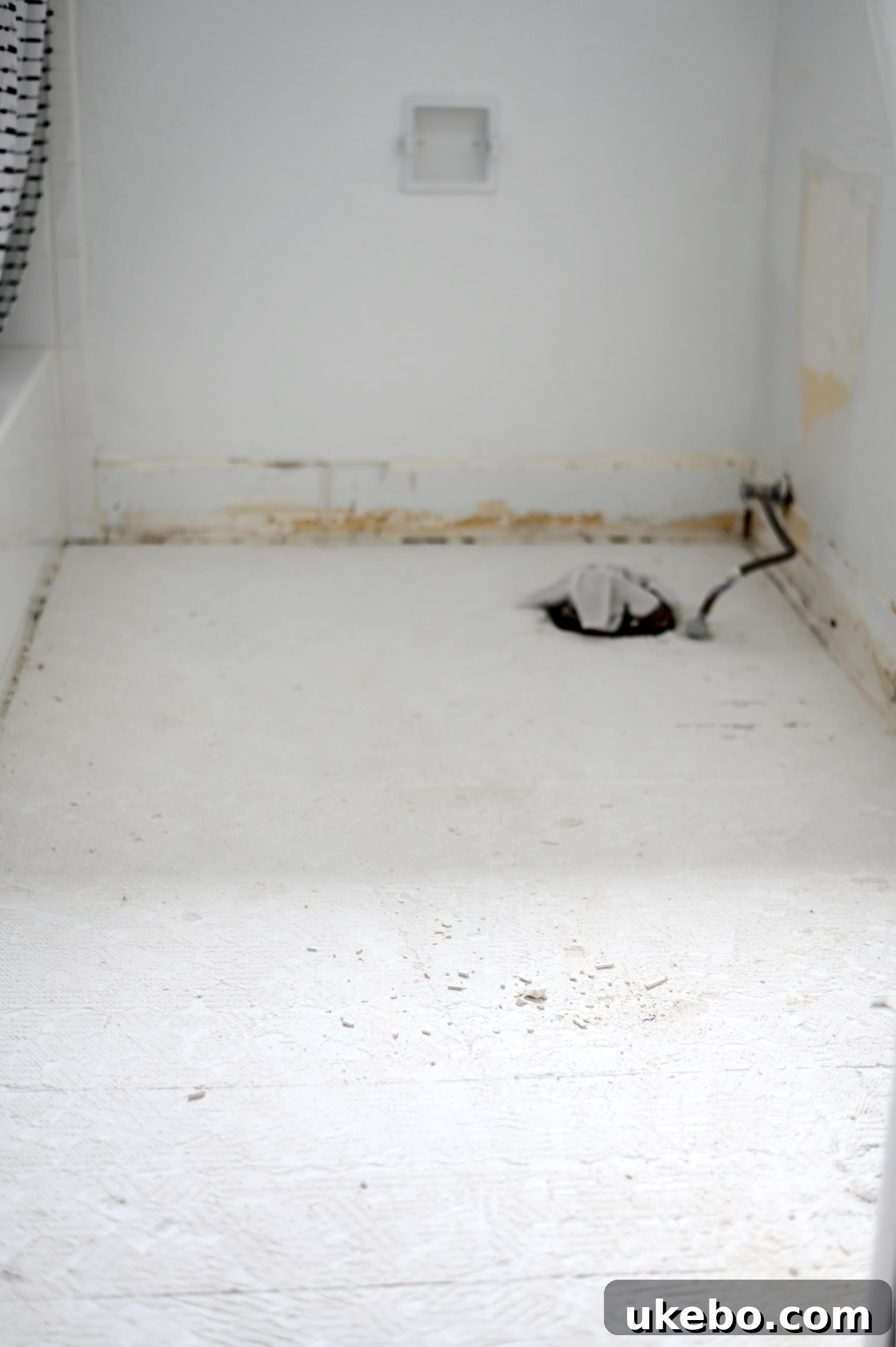 A closer view of the bathroom floor during tile removal, revealing the subfloor beneath.