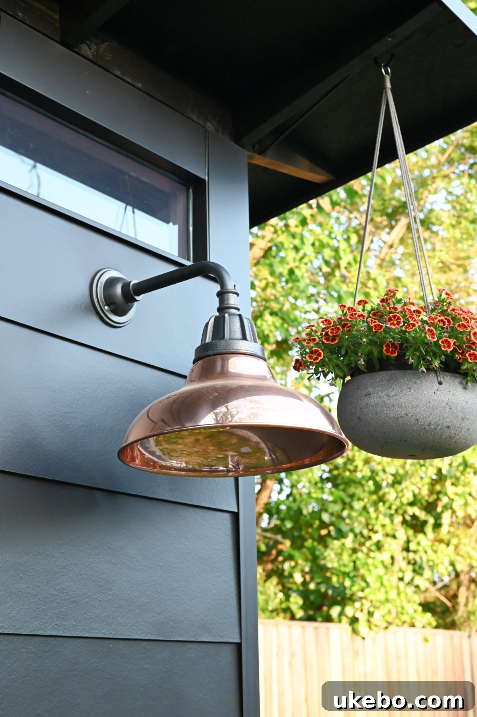 Finished exterior of the black backyard studio with copper Carson lights, cement planters with yellow roses, and pea gravel.