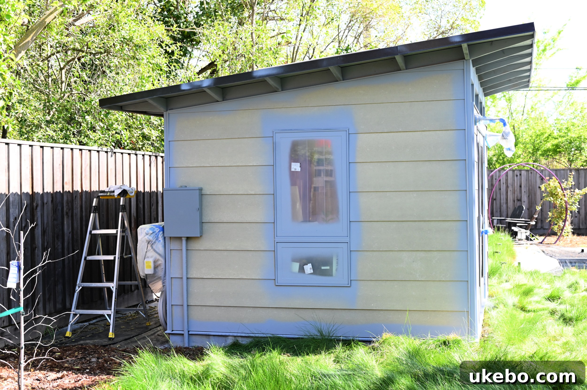 Applying Sherwin-Williams Multi-Purpose Latex Primer tinted gray to the studio eaves and trim using a handheld sprayer.